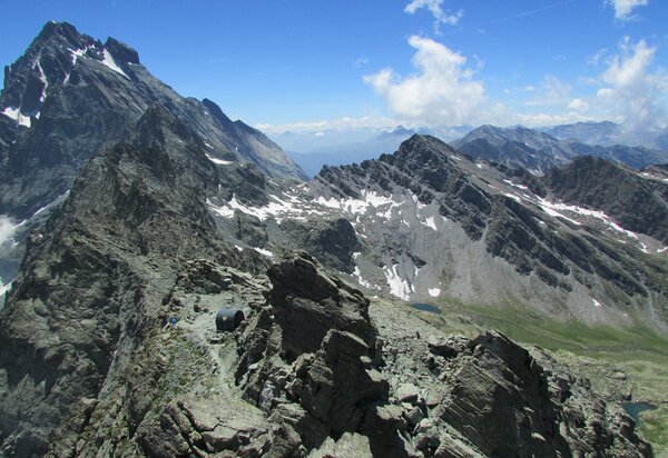Sulla sinistra la cima del Monviso, spruzzata di neve, piuù in basso le altre cime, in centro un bivacco. A destra più a valle due laghi
