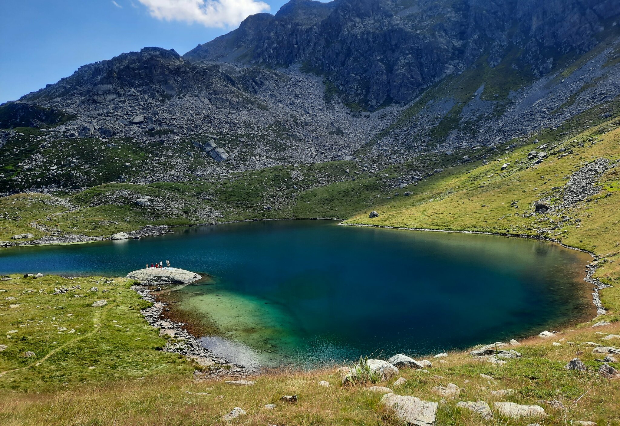 lago alpino blu e verde smeraldo circondato da prati e montagne