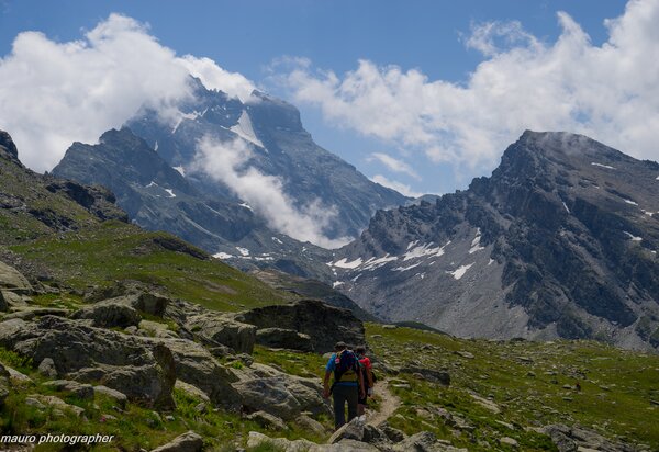 Escursionisti sul sentiero tra praterie alpine, sullo sfondo il Monviso con il dado di vallanta