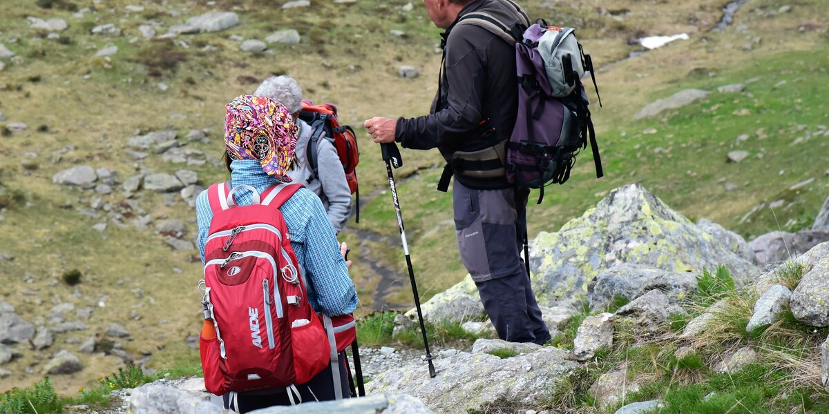 tre escursionisti di spalle, mentre parlano tra loro: tutti hanno zaino e bastoni da camminata