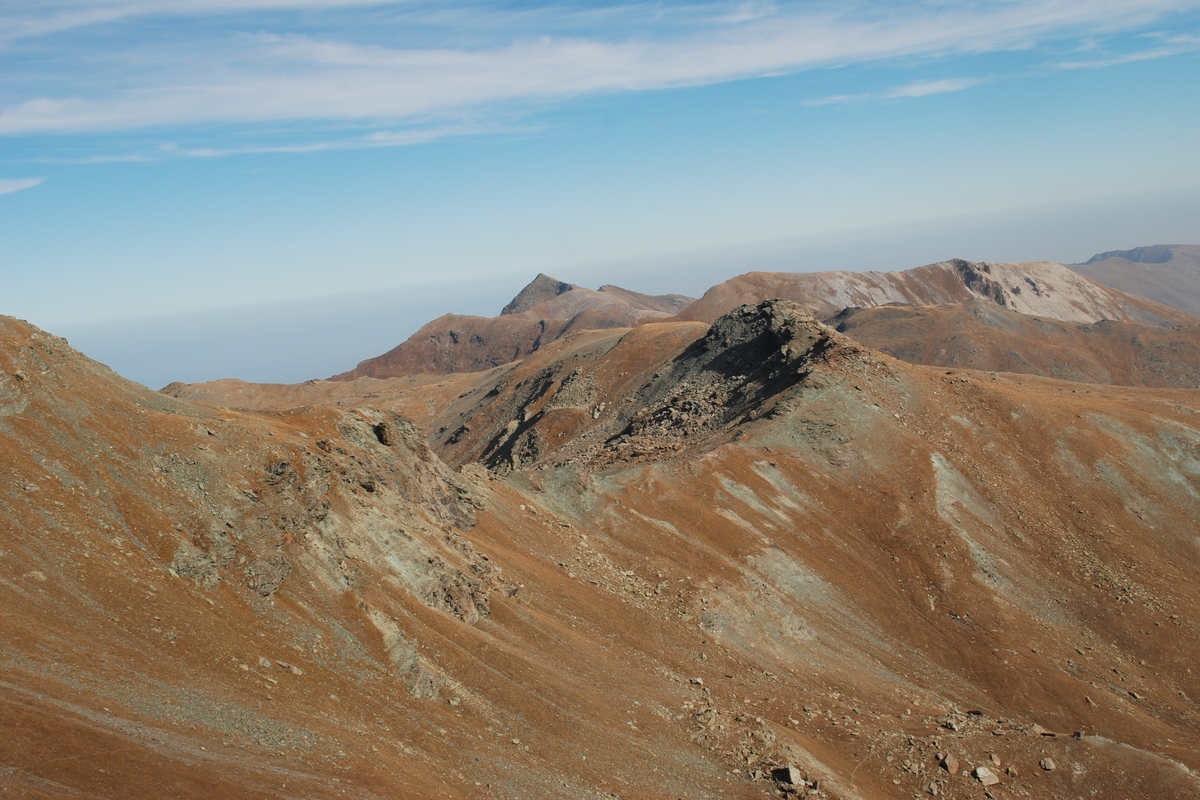 Pendii con prati già secchi e alcune dorsali alpine. cielo azzuzzo con qualche nuvola
